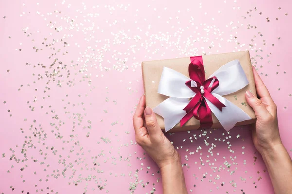 Cadeau ou boîte cadeau avec un grand arc dans les mains d'une femme sur une table rose. Composition Flatlay pour l'anniversaire de Noël, la fête des mères ou le mariage. — Photo