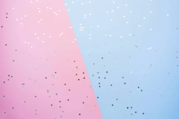 Confetti of gold stars glisten on a pink blue background. Festive holiday pastel backdrop.