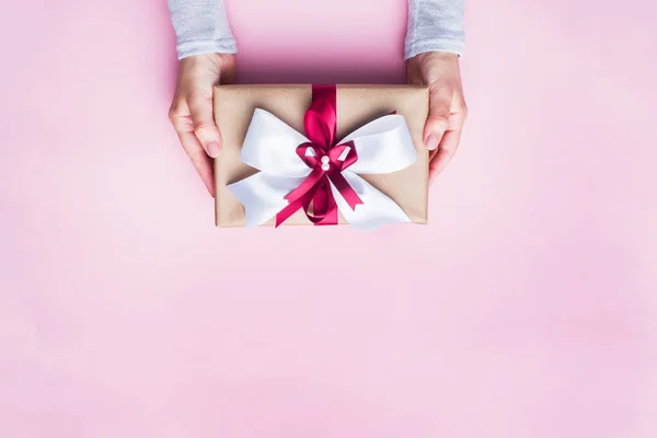 Cadeau ou boîte cadeau avec un grand arc dans les mains d'une femme sur une table rose. Composition Flatlay pour l'anniversaire de Noël, la fête des mères ou le mariage. — Photo