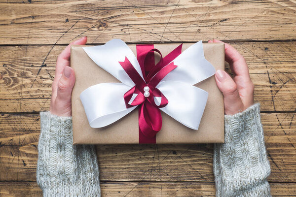 Подарочная коробка с большим бантиком в руках женщины в свитере. Плоская композиция на Рождество, День матери или свадьбу
.