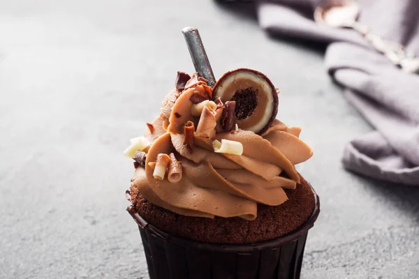 Schokoladenmuffin mit Sahne, verziert mit Bonbons und Schokoladenstücken. dunkler Betonhintergrund. Kopierraum. — Stockfoto