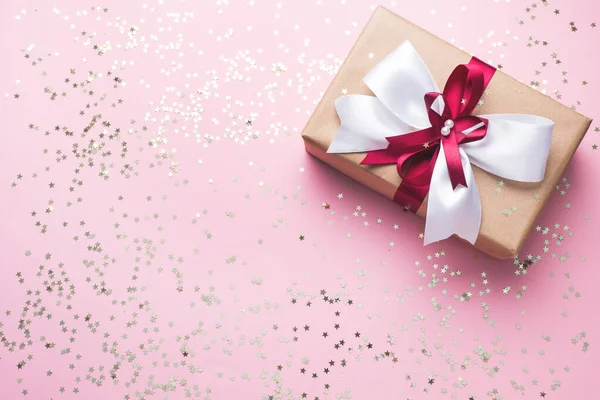 Fond rose festive avec des étoiles confettis scintillantes. Coffret cadeau avec un bel arc. Espace pour le texte et votre produit . — Photo