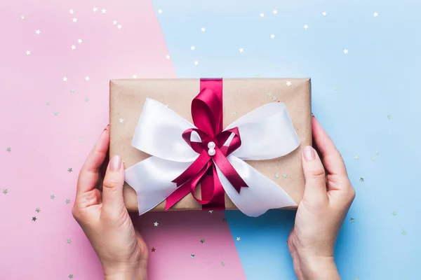 Coffret cadeau ou cadeau avec un gros noeud dans les mains d'une femme sur une table rose bleue. Composition Flatlay pour l'anniversaire de Noël, la fête des mères ou le mariage . — Photo