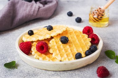 Beton bir arka plan üzerinde taze ahududu ve yaban mersini ile oluklu waffle çerezleri. Kopyalama alanı.