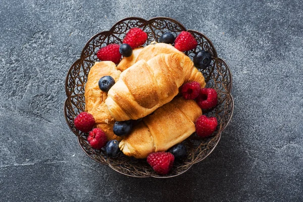 Croissants con frambuesas frescas y arándanos sobre un fondo de hormigón oscuro. Copiar espacio. concepto de desayuno café miel . — Foto de Stock