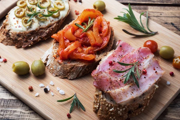 Sandwichs au pain complet avec fromage à la crème, bacon et olives poivrons en conserve avec tomate sur fond en bois. — Photo