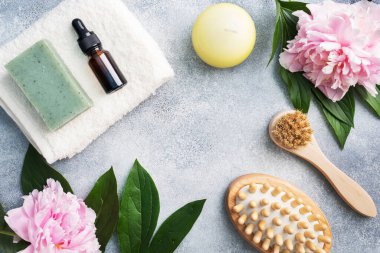 SPA ve Refah kavramı. Masaj fırçası, kozmetik yağlar ve sabun. Şakayık çiçekli hafif bir arka plan. Boşluğu kopyala