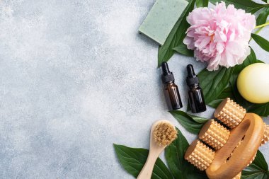 SPA ve Refah kavramı. Masaj fırçası, kozmetik yağlar ve sabun. Şakayık çiçekli hafif bir arka plan. Boşluğu kopyala