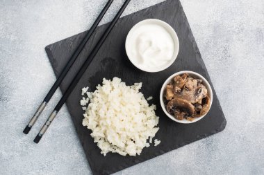 Siyah bir büfede çubuklarla kaynamış beyaz pirinç ve ekşi krema. Gri beton arkaplan Boşluğu kopyala.