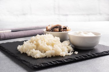 Siyah bir büfede çubuklarla kaynamış beyaz pirinç ve ekşi krema. Gri beton arkaplan Boşluğu kopyala.