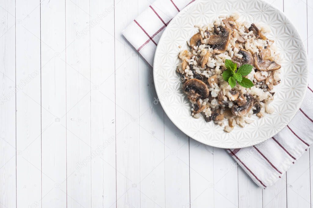 Risotto with mushrooms on a white plate. Boiled white rice with champignons in cream sauce. Light wooden background. Copy space