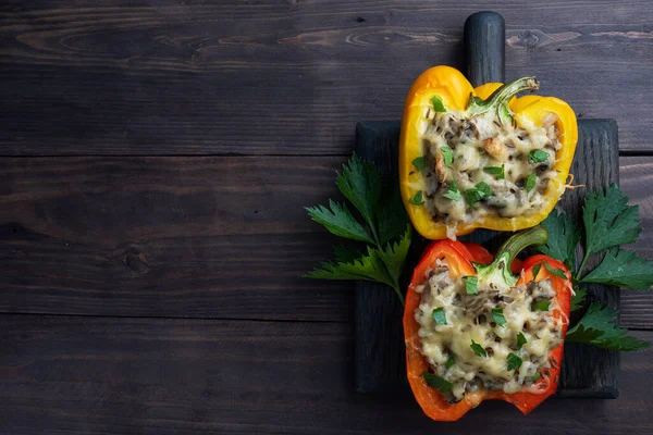 Pimentos doces recheados com cogumelos de arroz e queijo com ervas. Metades assadas de pimentas vermelhas e amarelas com recheio. Fundo de madeira escuro. Espaço de cópia , — Fotografia de Stock