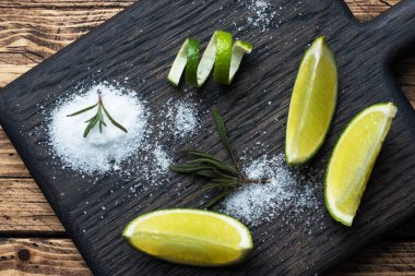 Tahta kesme tahtasında taze limon, tuz ve biberiye dilimleri..