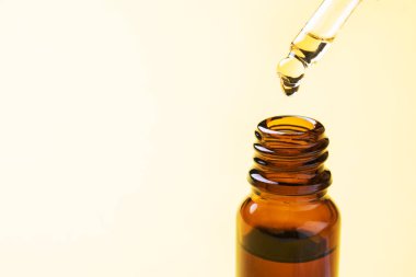 Damlalar pipetten düşer. Sarı arka planda pipetli bir şişe kozmetik yağı. Uzayı kopyala Seçici odak.