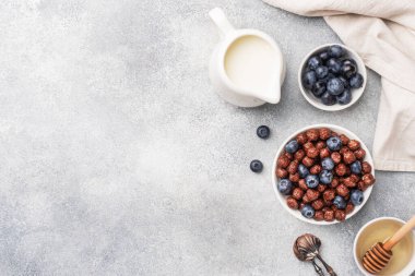 Doğal mısır gevreğinden yapılmış çikolata taneleri taze yaban mersini, bal ve süt. Sağlıklı sağlıklı bir kahvaltı konsepti. Boşluğu kopyala Gri arkaplan