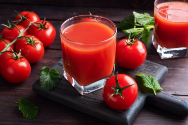 Cam bardakta domates suyu ve dalda taze olgun domates. Kopya alanı olan koyu tahta arkaplan.