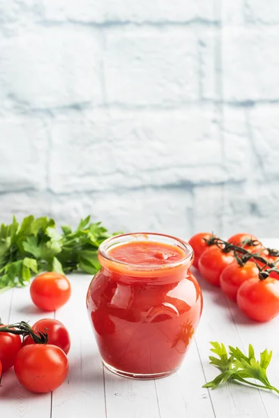 Tomatoes in their own juice or Tomato paste in a glass jar and fresh tomatoes on a white wooden table Copy space