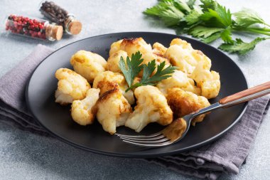 Kızarmış karnabahar çiçekleri siyah bir tabakta hamurda. Gri beton arkaplan