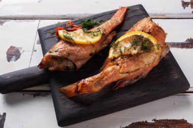 Beyaz ahşap arka planda dosyalamak için ahşap tahtada domates biberli levrek ve şifalı otlar. Fırında pişirilmiş levrek balığı.