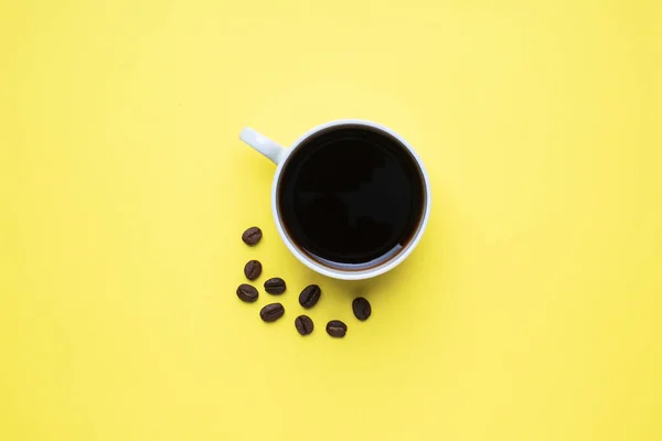 杯子里的黑咖啡和黄色背景的咖啡豆。顶视图复制空间. — 图库照片