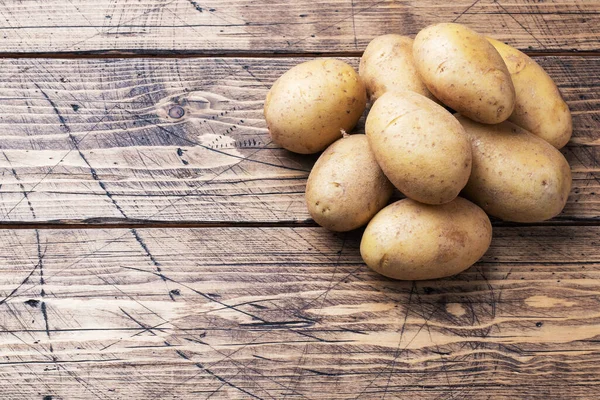 Several tubers of raw potatoes on a wooden background. Copy space.