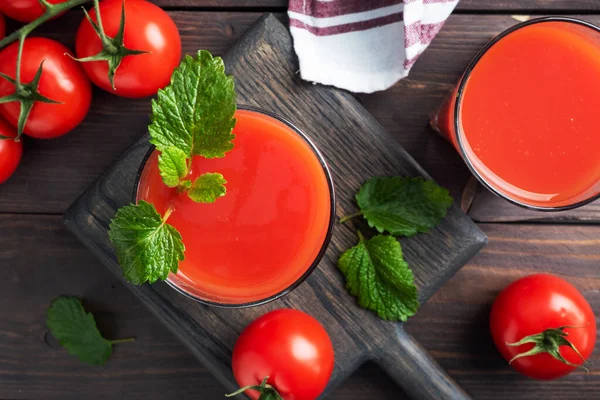Tomato juice in glass glasses and fresh ripe tomatoes on a branch. Dark wooden background with copy space. — Stock Photo, Image