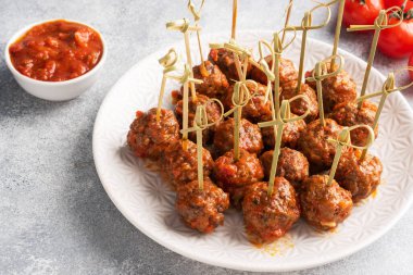 Biftek köfteleri, barbekü şişlerinde bir tabakta domates sosuna bulanmış. Hafif beton arkaplan.