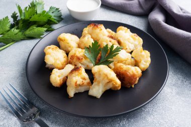 Kızarmış karnabahar çiçekleri siyah bir tabakta hamurda. Gri beton arkaplan.