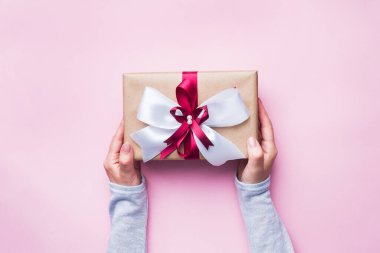 Pembe masadaki bir kadının elinde büyük bir fiyonk olan hediye ya da hediye kutusu. Noel için yassı beste, Anneler Günü ya da düğün.