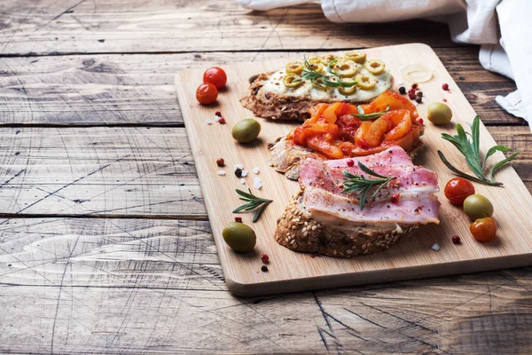Sandwichs au pain complet avec fromage à la crème, bacon et olives poivrons en conserve avec tomate sur fond en bois. Espace de copie. — Photo