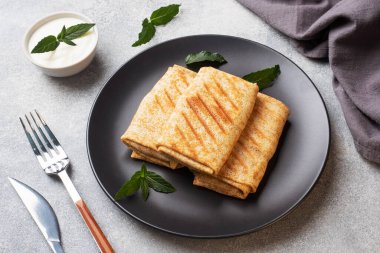 Ekmeğe sarılmış ince krepler siyah bir tabakta nane şekeriyle kızartılıyor..