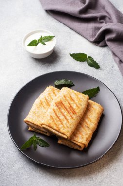 Ekmeğe sarılmış ince krepler siyah bir tabakta nane şekeriyle kızartılıyor..