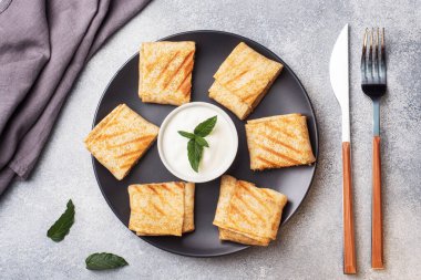 Ekmeğe sarılmış ince krepler siyah bir tabakta kızartılır. Nane yapraklı krema sosu..