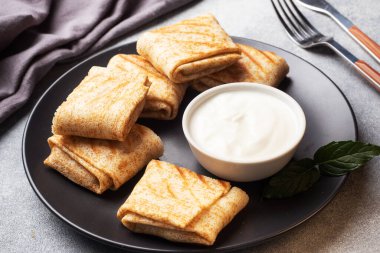 Ekmeğe sarılmış ince krepler siyah bir tabakta kızartılır. Nane yapraklı krema sosu..