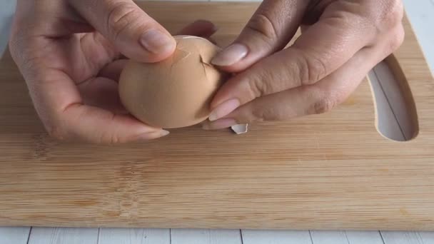 Les mains féminines se rapprochent et nettoient l'œuf de poulet bouilli. Home cuisine table en bois. — Video