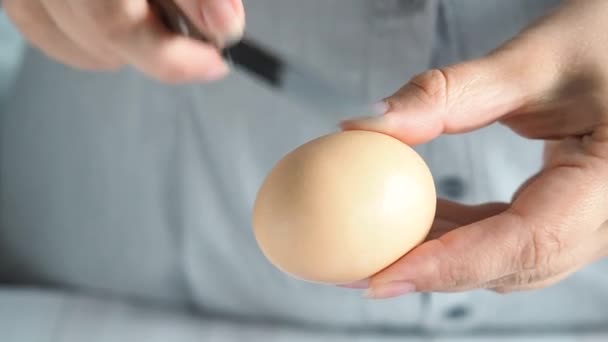 Uma cozinheira quebra um ovo de galinha com uma faca. — Vídeo de Stock