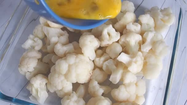 Inflorescencias de coliflor en una bandeja para hornear. El cocinero vierte huevo crudo batido sobre la coliflor. — Vídeos de Stock