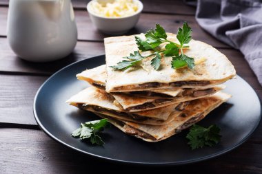 Peynirli ve mantarlı Quesadilla parçaları maydanoz yapraklı bir tabakta. Ahşap arkaplan kapat
