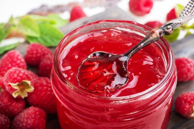 Cam kavanozda ev yapımı ahududu reçeli ve ahşap bir arka planda naneli taze ahududu..