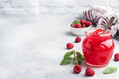 Cam kavanozda ev yapımı ahududu reçeli ve gri arkaplanda naneli taze ahududu. Boşluğu kopyala.