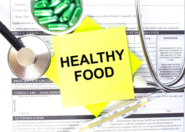 Text Healthy Food in a notebook on medical forms with a phonendoscope and green pills. Medical conzept