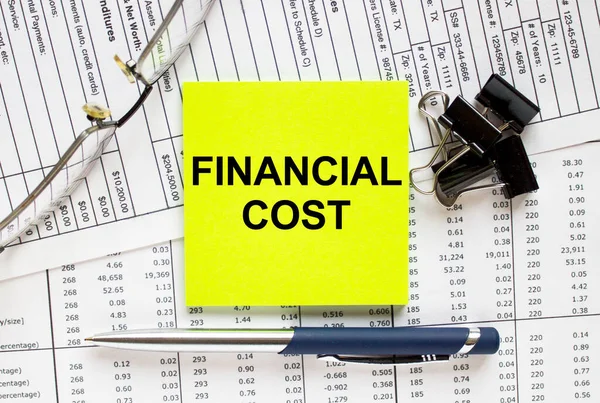 Text Financial Cost on financial tables with pen, glasses and paper clips. Business and financial conzept