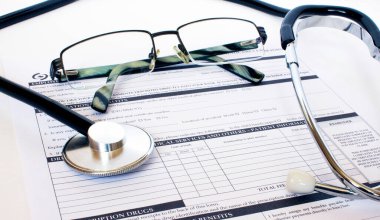 Masada steteskop ve gümüş gözlüklerle duran reçete formu. İlaç ya da eczane kavramı.