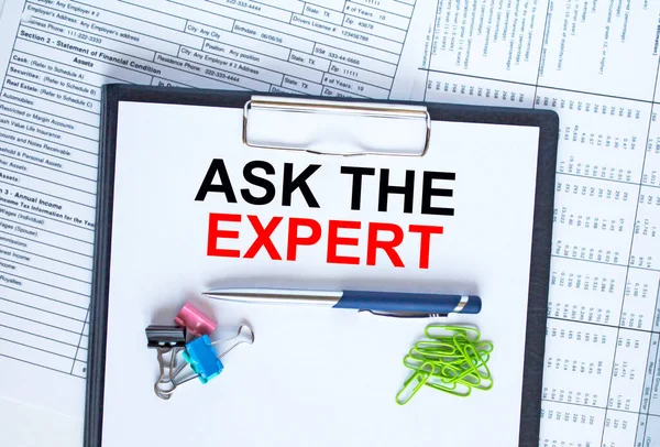 Text Ask The Expert on folder with clip. Pen with paper clips on financial table. Business and financial concept