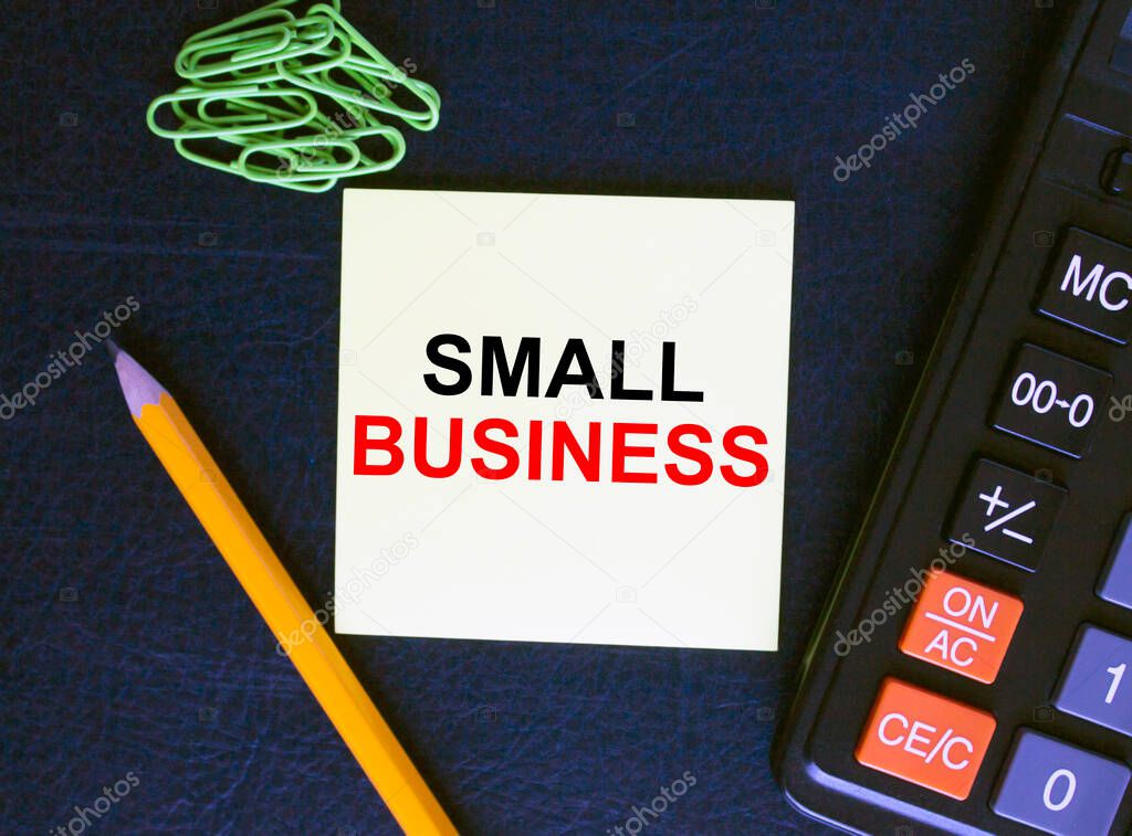 Yellow sticker with text Small Business on black baground with calculator, pencil and paper clips. Business concept photo