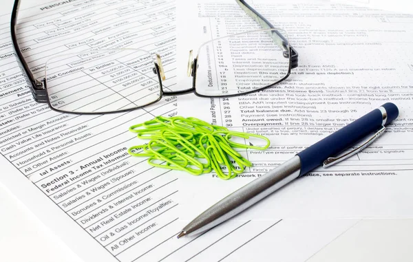 A blue metal pen sits on the financial tables with green paper clipsand eyeglasses. Business and financial concept