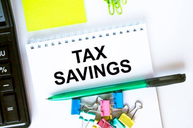 Metin Vergi Tasarrufları ile not defteri. Hesap makinesi, yeşil kalem etiketleri ve kırtasiye klipsleri. İş ve mali konsept