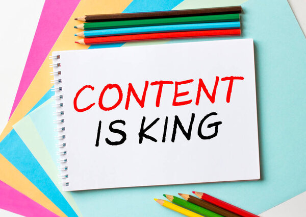 Блокнот с текстом Content Is King находится на цветной бумаге с цветными карандашами. Концепция фото
