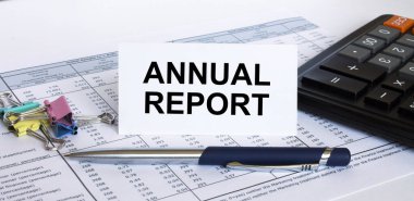 Finans masasında mavi metal kalem, hesap makinesi ve ataç bulunan beyaz kart hakkındaki yıllık metin raporu. İş ve mali konsept
