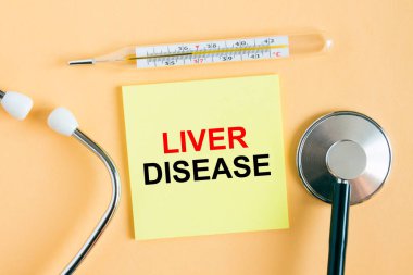 Üzerinde karaciğer hastalığı yazan sarı etiket. Sıcak bir arka planda fonendoskoplu bir termometre. Tıbbi konsept fotoğrafı olarak kullanılabilir.